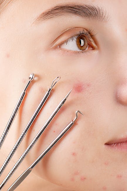 Close-up image of a person's face showing their right eye, with fair skin, brown iris, and minimal makeup. Several professional stainless steel extraction tools with different angled hooks and loops are positioned against their cheek and jawline, indicating a facial skin treatment or extraction process. The background is neutral and out of focus, emphasizing the skin and tools. This detailed visual relates to skincare procedures commonly performed in cosmetic or dermatology settings, which may be part of home or professional facial treatments. The lighting is soft and even, highlighting the skin's surface and the metallic sheen of the tools, aligning with professional skincare or cosmetic services.